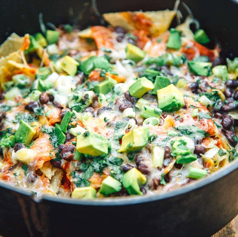 Campfire Nachos – no worries.
Loaded nachos is the perfect lazy meal to cook over the. Not only does it require minimum effort to put together, especially if you use tinned ingredients, but you also don’t need to do much washing up as it can eaten out of the tray using fingers. This blog will detail how you can go about making nachos in a dutch oven and, if you don’t have a dutch oven, how to make them in an aluminium tray over the campfire.  

The dutch oven method 

Dutch ovens are a great addition to your camping equipment. 

To use a dutch oven, you need to heat up around 18 coals. 

You then place the dutch oven over two thirds of these coals, and place the leftover third of coals on top of the lid. They work by heating the food from on top as well as underneath, basically acting like a normal oven. Although for this recipe, you don’t need to place coals on the lid, just to place a lid or some foil on your dutch oven, cast iron skillet, or aluminium tray in order to melt the cheese.   

To make nachos in a dutch oven, I would recommend starting by lining the bottom and sides of the oven with foil or baking paper. Although this step isn’t essential its really useful for a much easier clean-up. Then lightly oil the bottom of the pan with some neutral oil- this will stop the nachos from sticking together. 

To make this recipe you will need around 500g tortilla chips and around 200g passata, or any kind of Mexican style chilli tomato sauce.   

You will also need 120g grated cheese, you can use a mixture of any semi-hard cheese you feel like, but cheddar does work well. 

To make this recipe you will also need a can of black or kidney beans, one large avocado- cut into chunks, 4-5 sliced spring onions and a handful of chopped coriander.  

Start by spreading a third of the tortilla chips on the bottom of the dutch oven. T

hen add a quarter of the tomato sauce, black beans and grated cheese, with a handful of the avocado, spring onions and coriander. 

Repeat this process for the second layer. 

Then build up the final layer using the remaining third of chips, half each of the tomato sauce, beans and cheese. 

Top with the remainder of the avocado, coriander and spring onions.   

Place the lid on the dutch oven and put it over your campfire or over coals. 

If you choose to cook over the campfire, make sure it has burnt down to the hot embers, as these emit a more controlled heat- trying to cook over flames will only result in your food getting burnt. 

The lid should trap steam in the dutch oven, melting the cheese and slightly softening the tortilla chips. 

If you don’t have a lid for your dutch oven, you can just use a sheet of aluminium foil or even a plate. You can also use a cast-iron skillet with a lid for this recipe. 

Cook for around 10 minutes until all the cheese has melted. 

Then serve with lime wedges, as the dutch oven will be very hot, using a large spoon to put portions of the nachos on plates for people to enjoy, instead of eating it straight out of the oven.  

For loads more tips on cooking over a campfire, and some tasty breakfast recipes, be sure to check out Campfire Breakfast in style.   

Cooking nachos in aluminium trays 

If you don’t have a dutch oven, then you can also cook nachos over the campfire in aluminium trays. 

Build the nachos in a large aluminium tray as you would in the dutch oven, layering until the tray is full. You could even make multiple trays of nachos if you’re cooking for multiple people. Or if you’re cooking for picky eaters who don’t like one part of the nachos topping you can super easily make a separate portion without that ingredient. 

For loads more tips on cooking for picky eaters check out, Camping Favourites for Fussy Eaters.   

Once you’ve finished assembling the nachos, place some aluminium foil on the trays, crimping it around the edges. Then place them on a wire rack over a campfire that has burnt down to the embers. 

Again, cook for around 10 minutes (although it depends on how hot your campfire is and how big the tray is), the nachos will be done once all the cheese has melted.  

Alternative ingredients 

If you’d like a healthier alternative to tortilla chips for your nachos, you can use sliced sweet potato instead. Although keep in mind the fact that the sweet potato will take a lot longer to cook than nachos made with tortilla chips. It can take around 30 minutes, but be sure to check as this depends on the heat of the fire.   You can also add some finely chopped tomatoes, onions, chillis and red or green peppers. Although you can add raw chopped onions, we like to sauté our onions first. If you want you can definitely add some meat to the nachos, just split it between layers like the rest of the fillings. Sauté the uncooked ground meat with some taco seasoning on a pan over your camping stove. Make sure it’s thoroughly cooked before building your nachos. You could also replace the ground meat with a vegetarian or vegan alternative.  

If you like food a bit spicier, you can also add some chillis. Like the onions, you could add these raw or sauté them before splitting between the different layers and sprinkling on top. You could also add jalapenos. The recipe above is more of a guide than a strict recipe, so feel free to experiment and add whatever you feel like!   I hope that this blog has inspired you to try making some nachos over the campfire on your next camping trip. It is the perfect lazy and tasty meal, ideal for enjoying around your campfire with a beer.